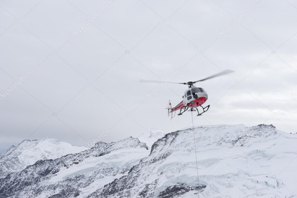 Guests standing near a helicopter on a snowy alpine ridge