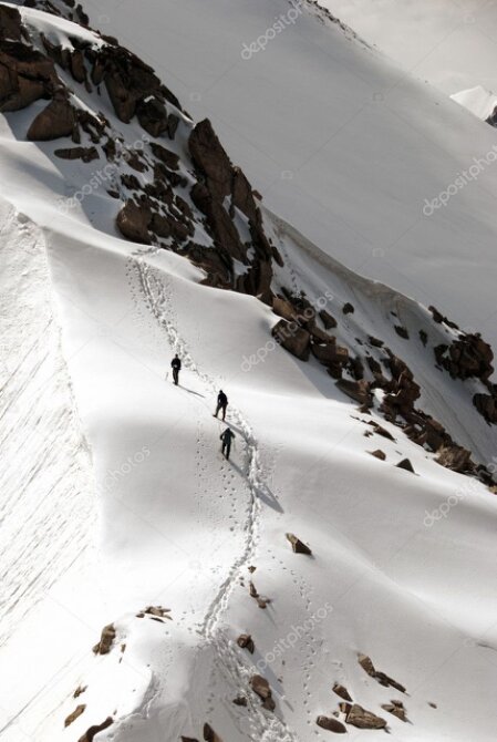 Small group hiking along an alpine ridge with snow-capped peaks in the distance