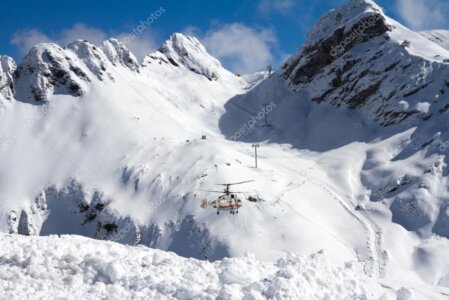 Helicopter landed on a snowy ridge with mountains in the background