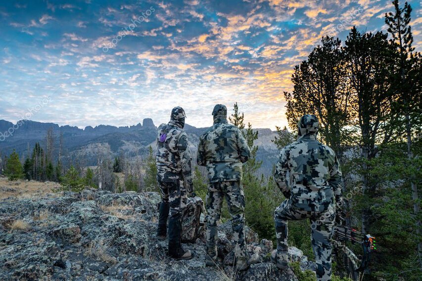 Silhouette of a hunter with binoculars on a high ridge at sunrise.