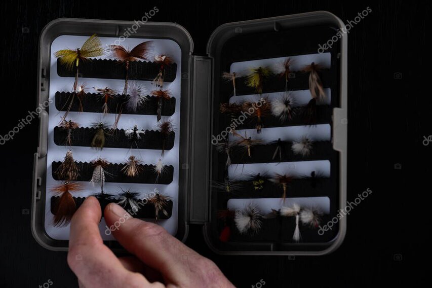 Open fly box and neatly laid-out gear on a camp table before heading out.