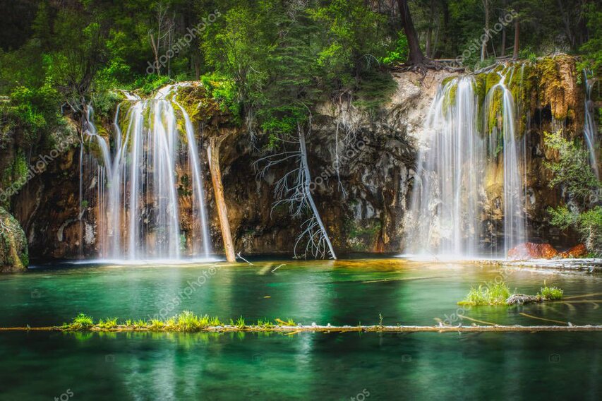 Hiker standing at a safe distance from a tall waterfall in a rocky canyon.