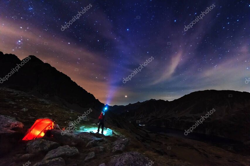 Overnight hiking camp with a glowing tent under a bright starry sky.